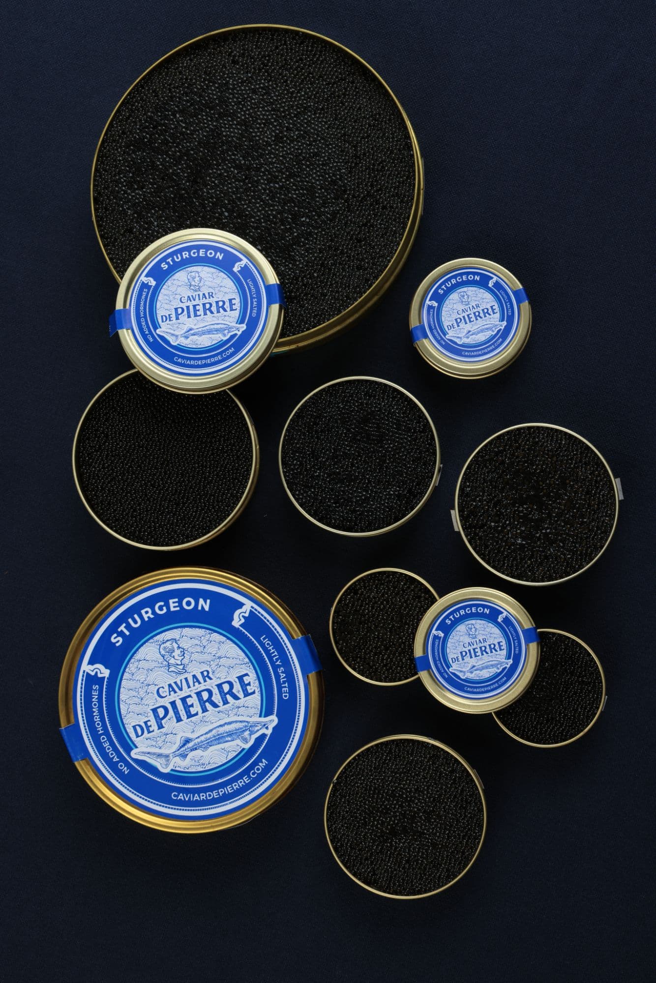 Open tins of Caviar De Pierre sturgeon caviar from above, on navy