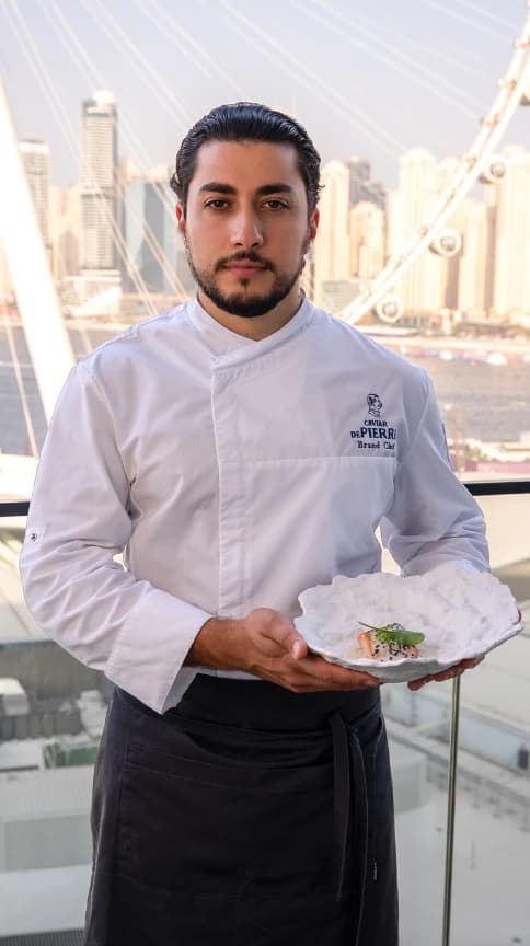 Rafael Gevorgyan, Brand Chef of Caviar De Pierre, holding a plated dish on a Dubai terrace