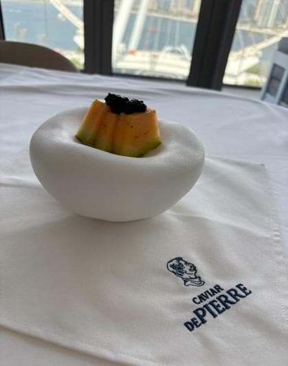 A neat block of cantaloupe topped with black caviar in a white bowl