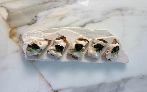 A row of sourdough canapés with sliced coconut, black caviar and dill