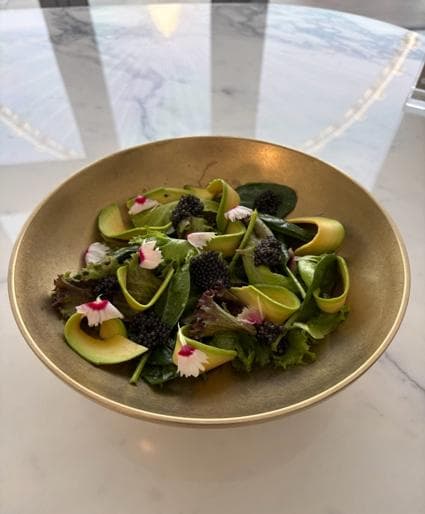 A bowl of mixed leaves with avocado, black caviar and edible flowers