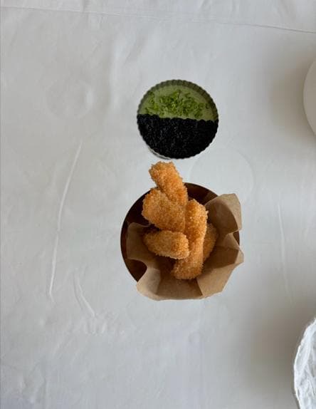 Crisp panko salmon sticks in a paper cone, with a dish of green sauce half covered in caviar