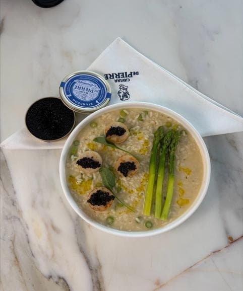 Asparagus risotto with seared scallops topped with black caviar, beside caviar tins