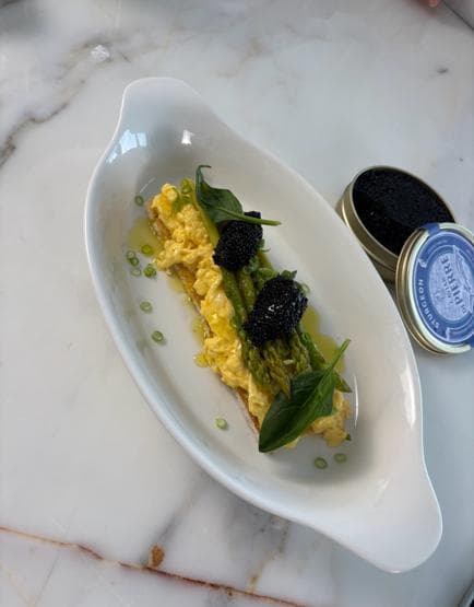Scrambled eggs on toast with asparagus and black caviar, beside two caviar tins