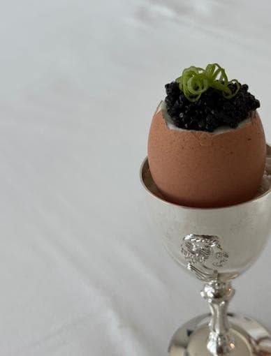 A soft-boiled egg in a silver egg cup, topped with black caviar and chives