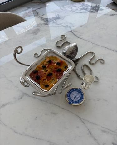 Thinly sliced tomatoes with black caviar in a silver dish shaped like an octopus
